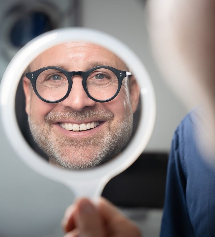 Patient betrachtet sein neues Lächeln im Spiegel – ästhetische Zahnbehandlung und Smile Design bei Dr. Hennies in Göttingen.“